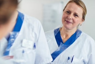 En kvinna i vit labbrock pratar med en annan kvinna.
